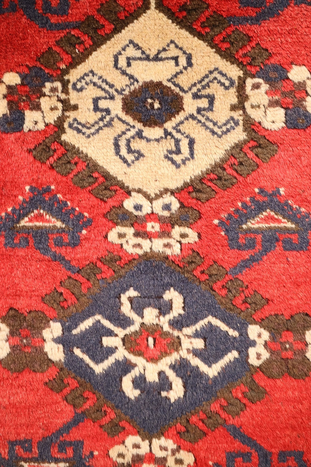 Détail des médaillons losangés crème et bleu à crochets du tapis Anadol rouge