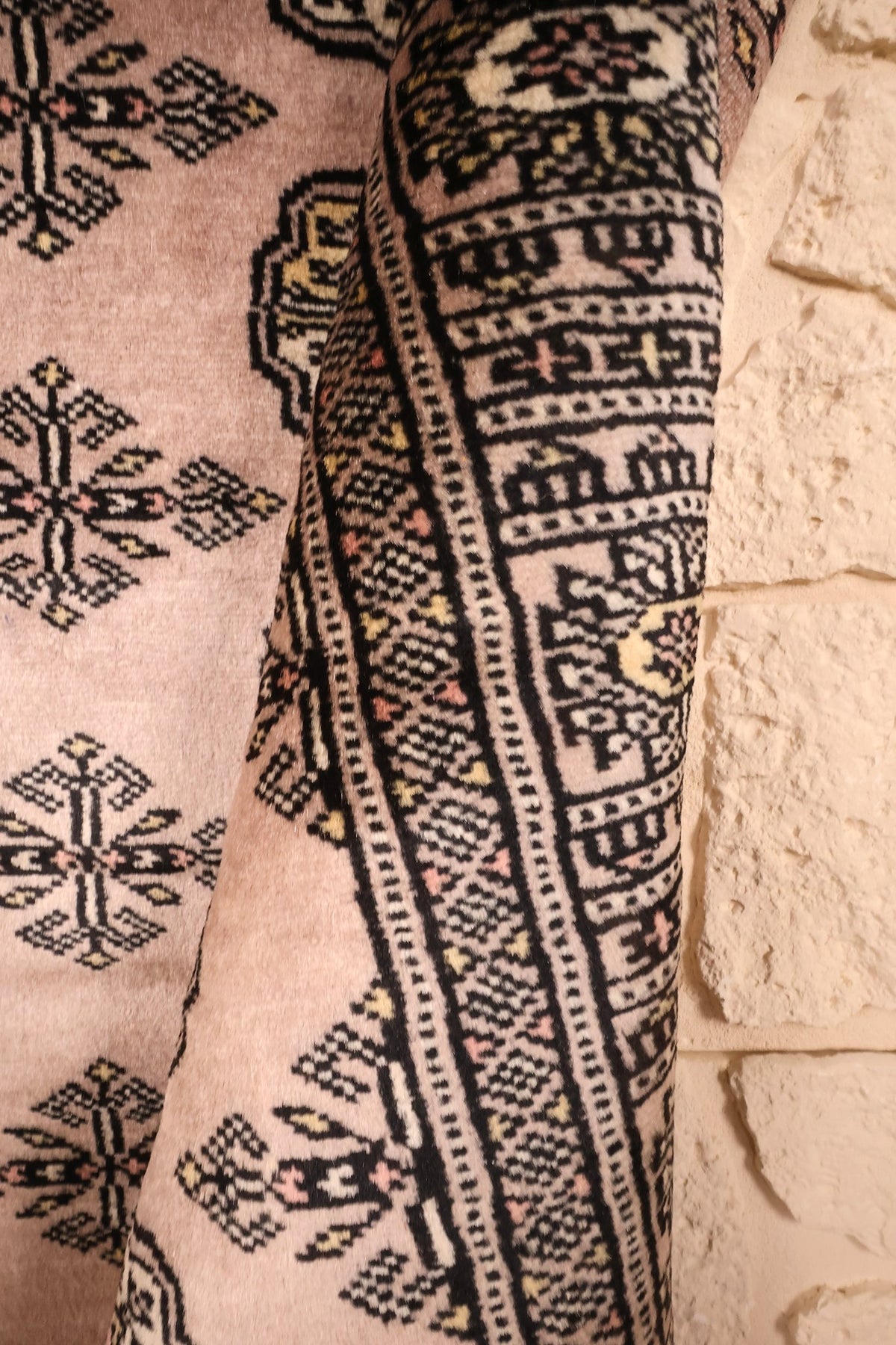 Angle du tapis Boukhara beige rosé, bordure en arceaux repliée contre le mur