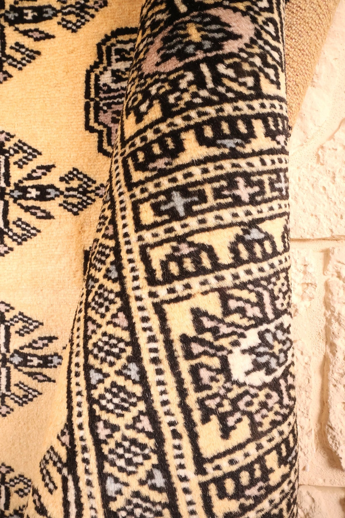 Coin replié du tapis Boukhara, galons noir et gris sur fond beige