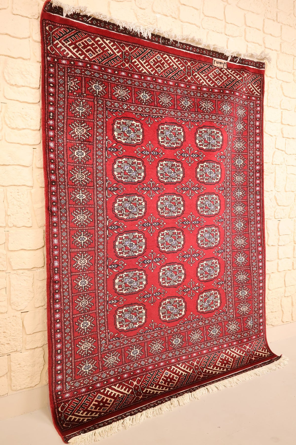 Tapis Boukhara rectangulaire en laine, vue de biais montrant le champ rouge et les franges