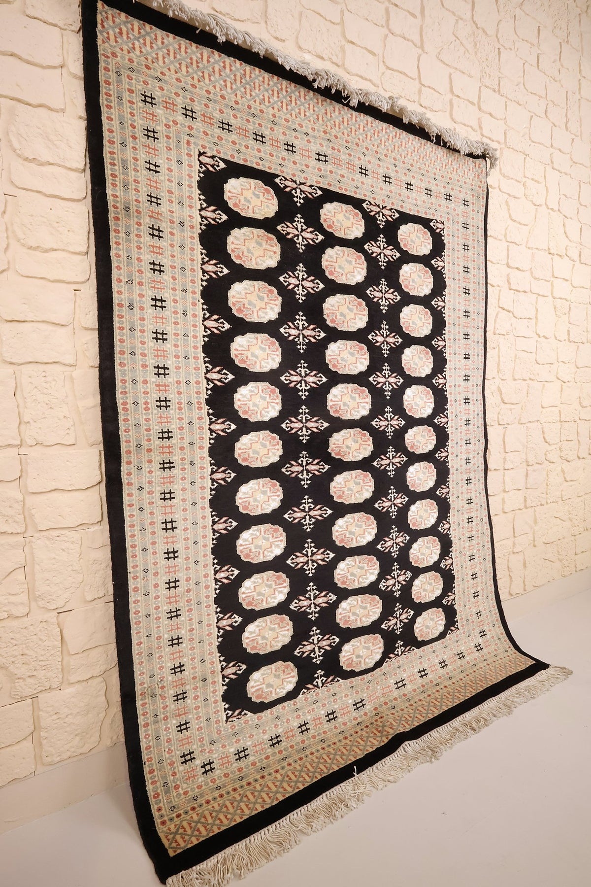 Tapis Boukhara rectangulaire en laine, vue de biais sur le champ noir et ses bordures claires
