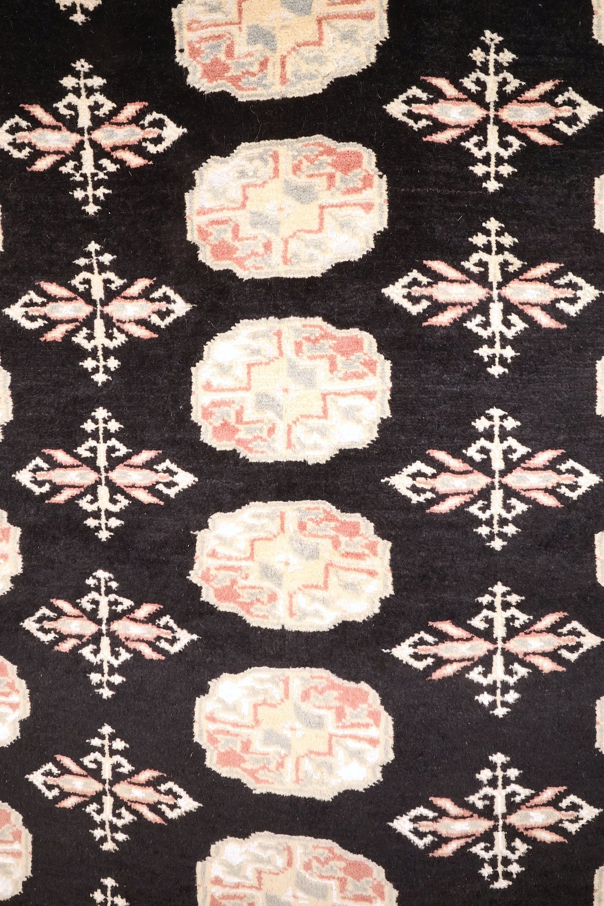 Détail des guls octogonaux beige et rose du tapis Boukhara sur fond noir