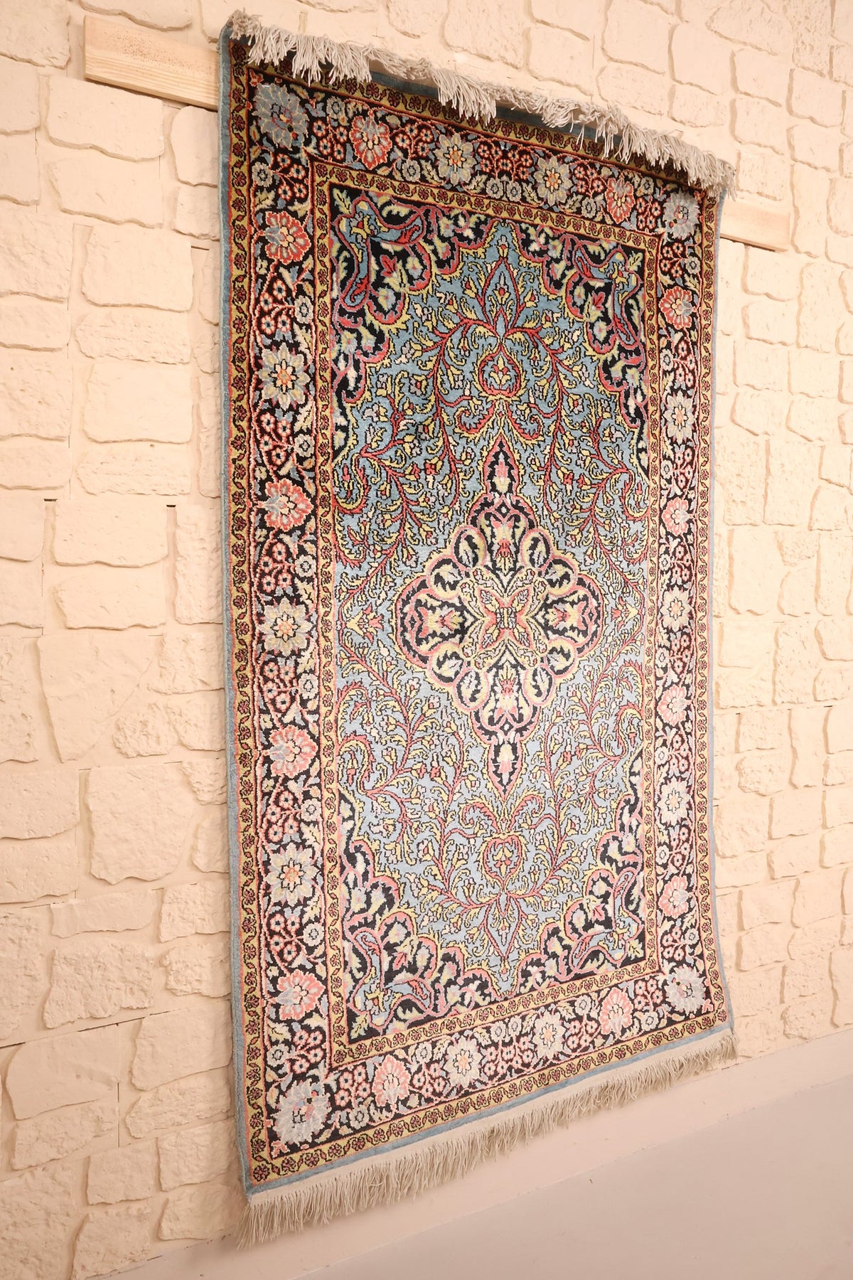 Tapis Cachemire bleu et rose en soie artificielle, vue de biais sur mur clair