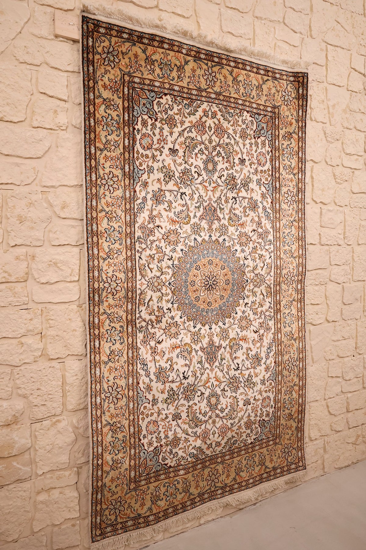 Tapis Cachemire beige et orange vu de biais, champ ivoire fleuri sur mur clair