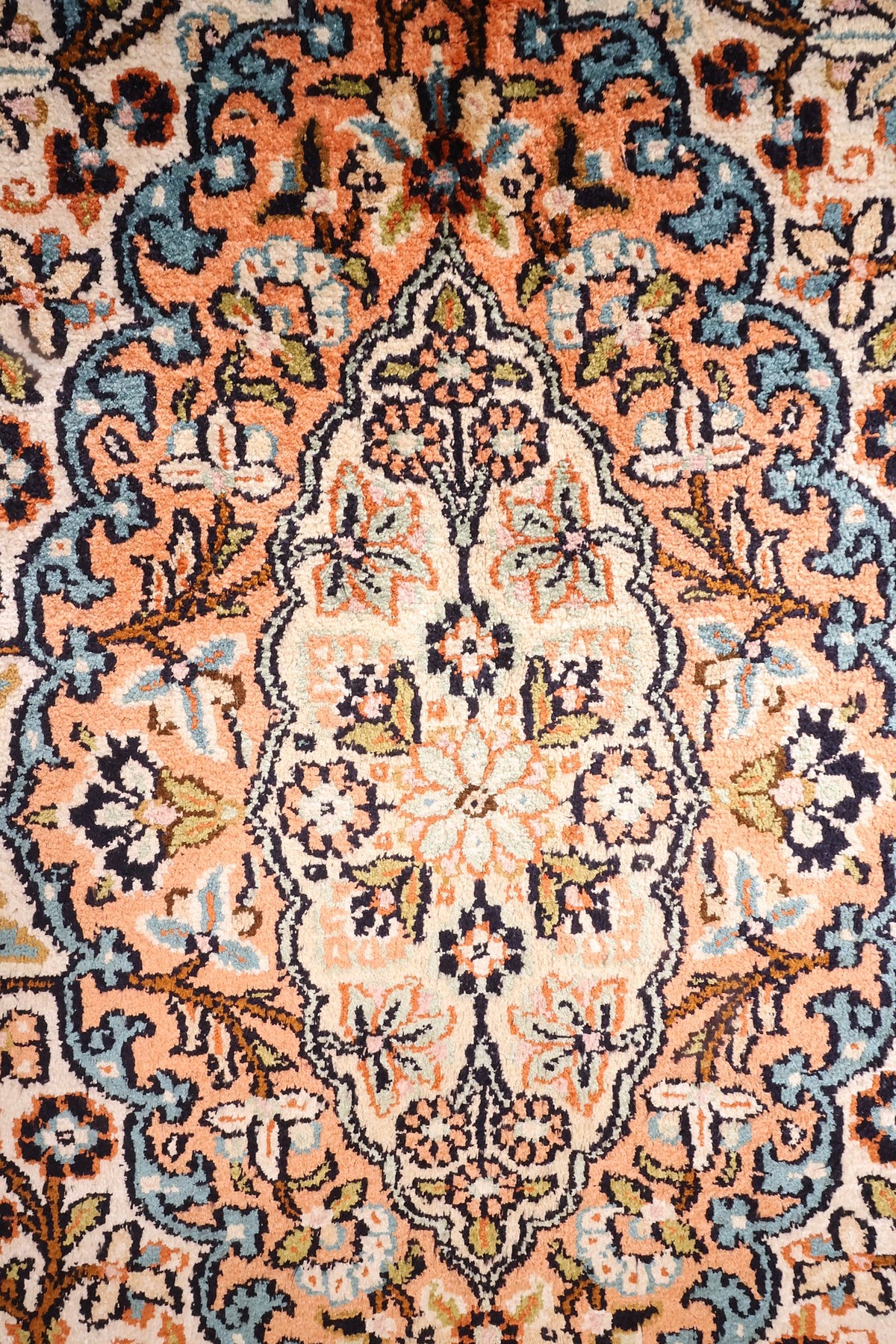 Détail du médaillon allongé saumon et bleu du tapis Cachemire beige