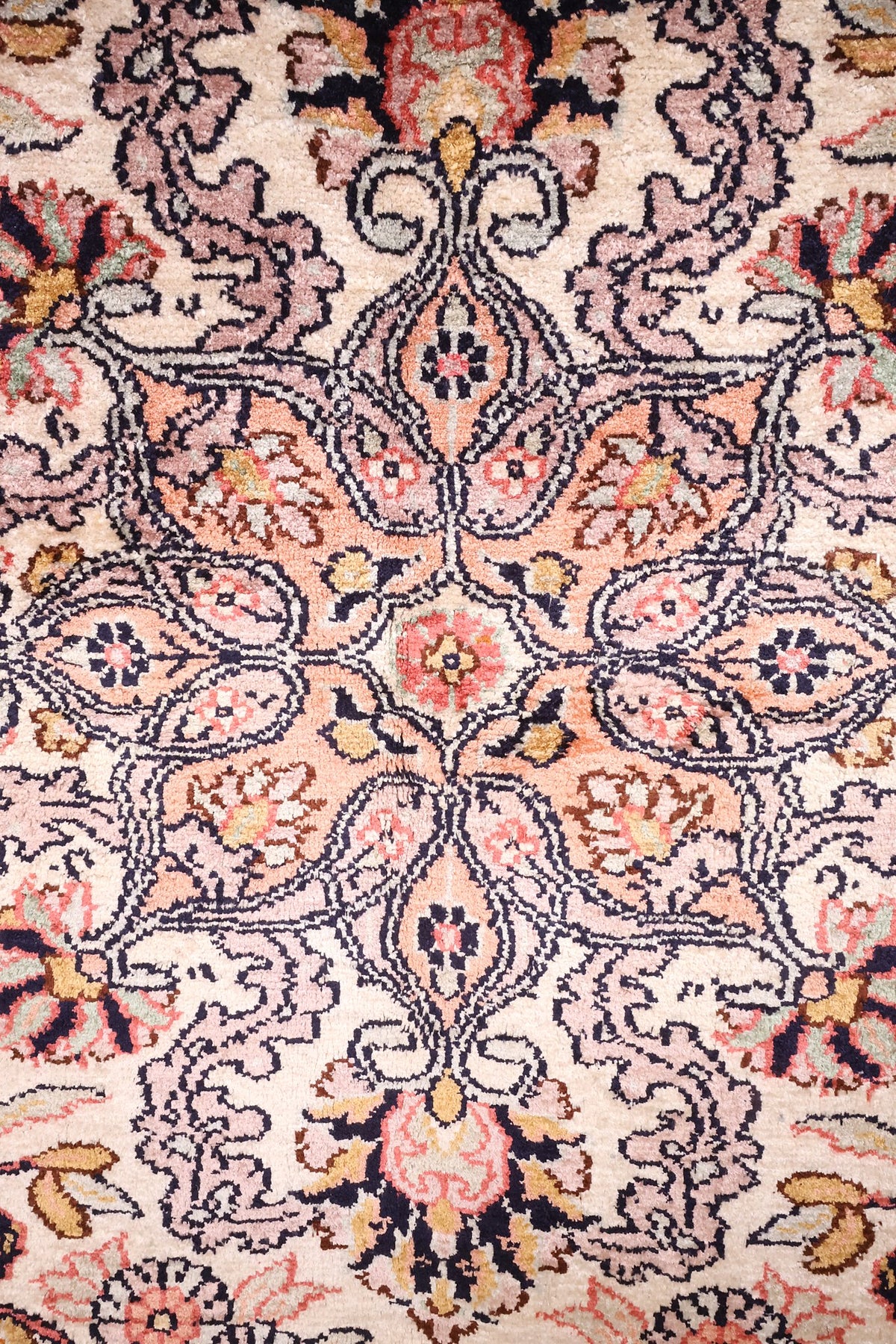 Détail du médaillon floral rose saumon et des rinceaux du tapis Cachemire
