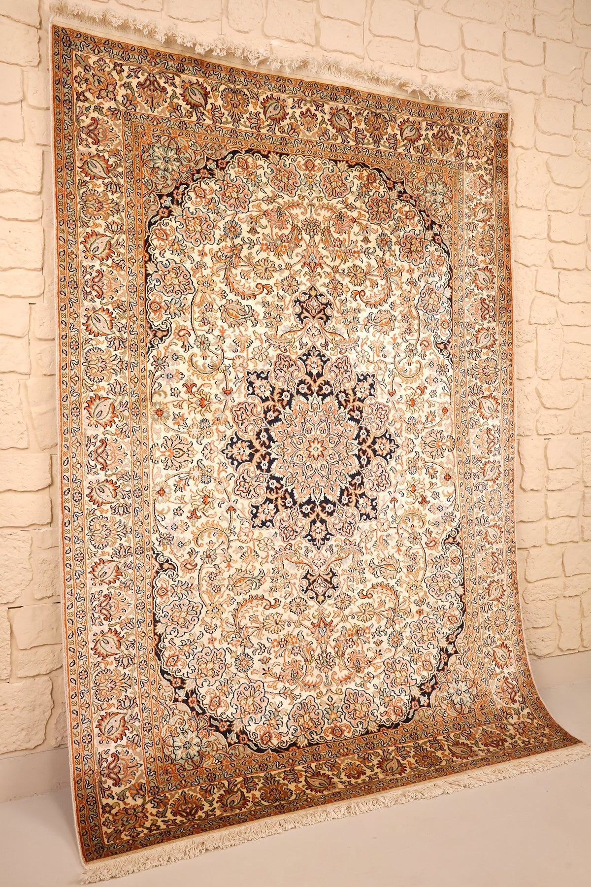 Vue de biais du tapis Cachemire en soie beige, franges claires et écoinçons sombres
