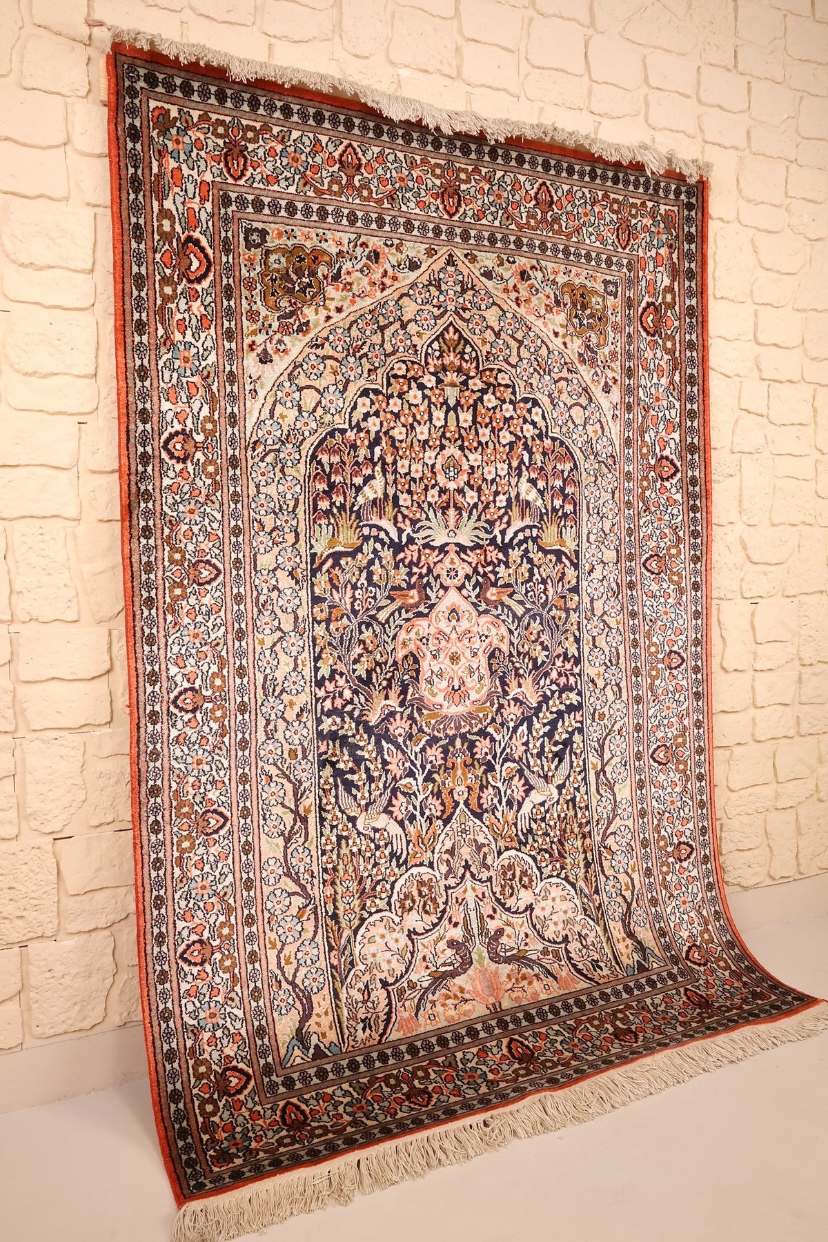 Tapis Cachemire en soie bleu et beige, vue de biais adossé au mur, franges blanches