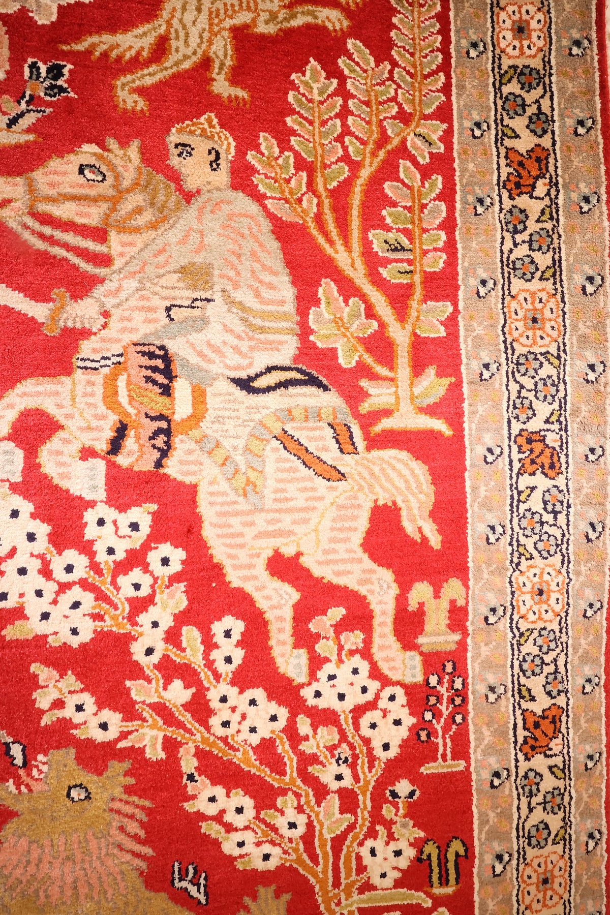 Bordure beige à rosettes orange et bleu nuit du tapis Cachemire, près d'un cavalier