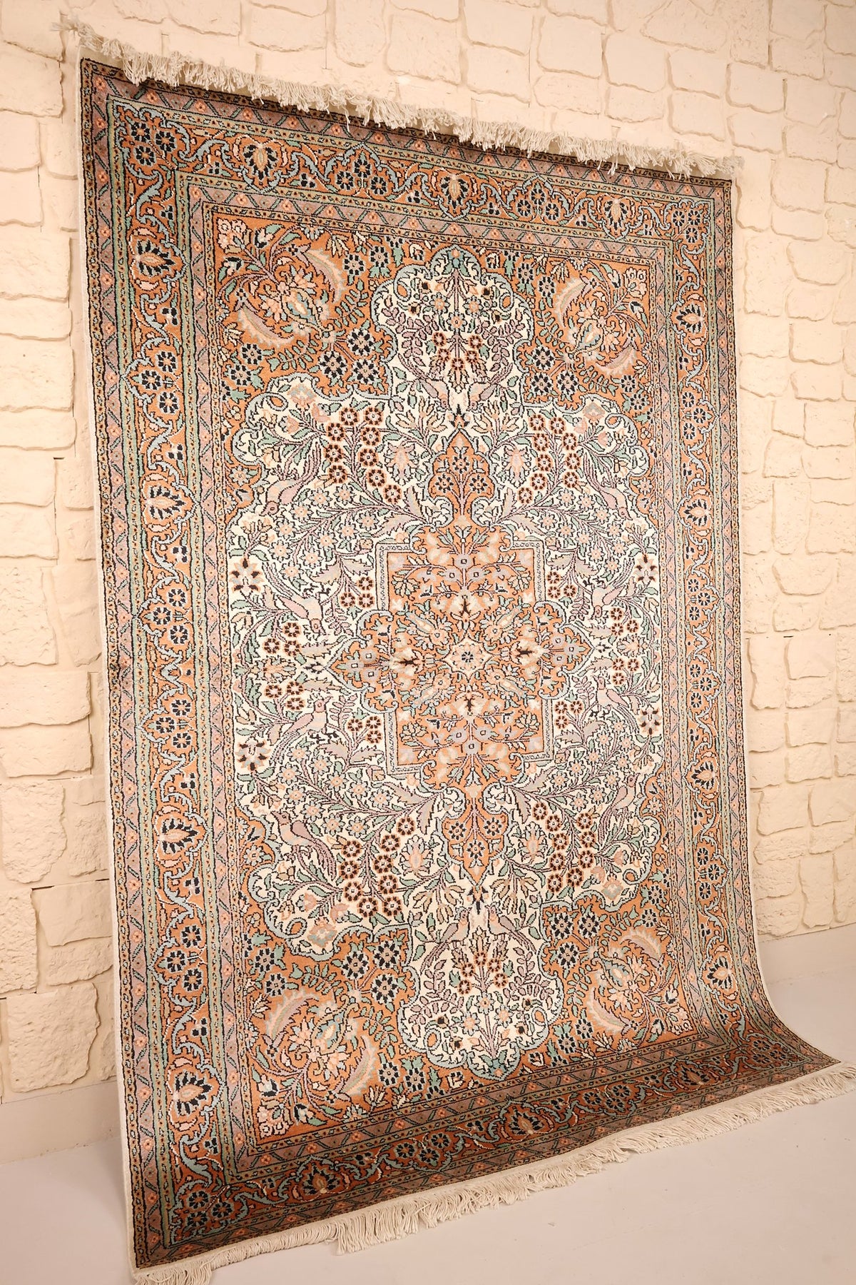 Tapis Cachemire en soie vu de biais, champ ivoire fleuri et médaillon central orangé