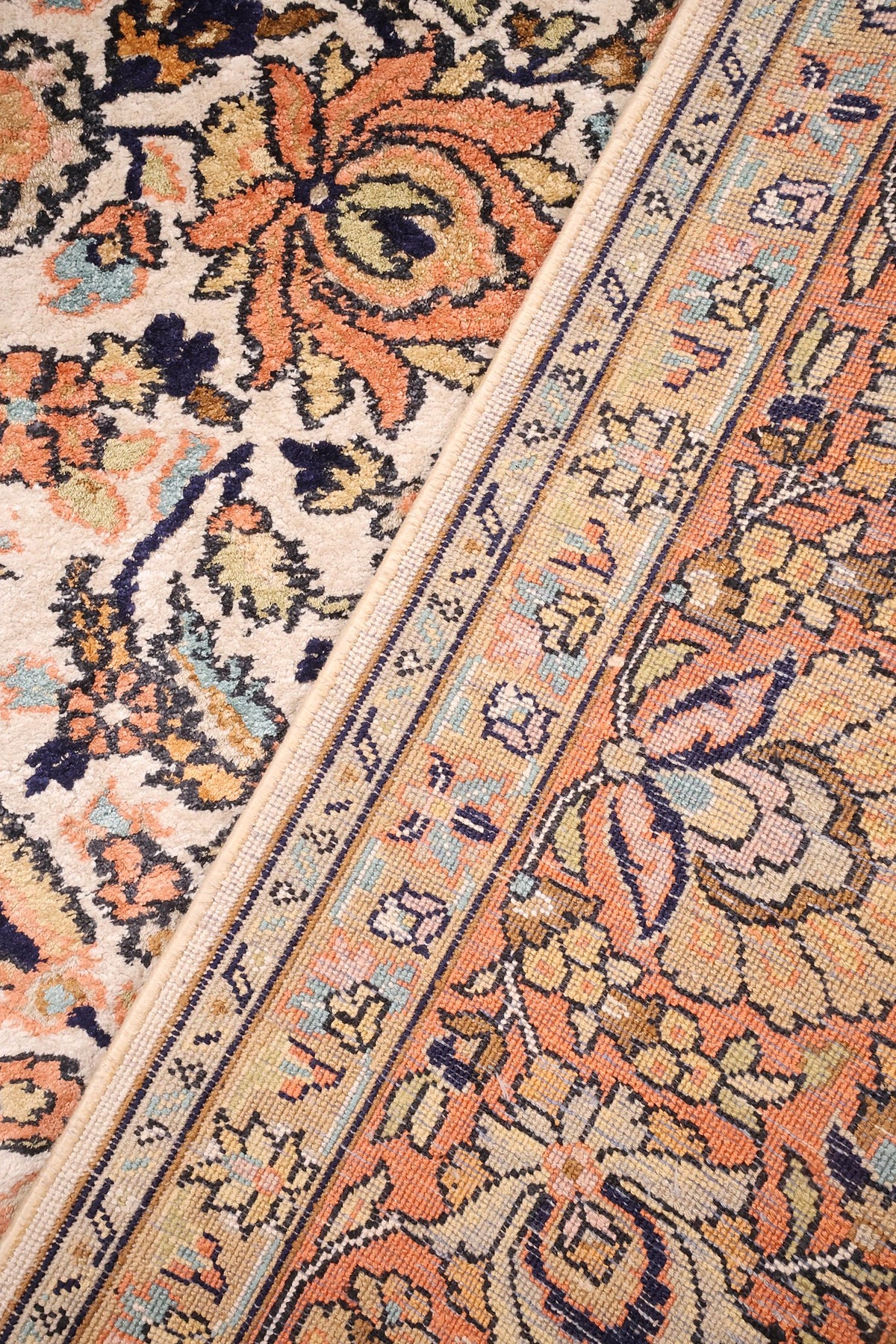 Coin replié du tapis Cachemire, passage du champ beige à la bordure fleurie