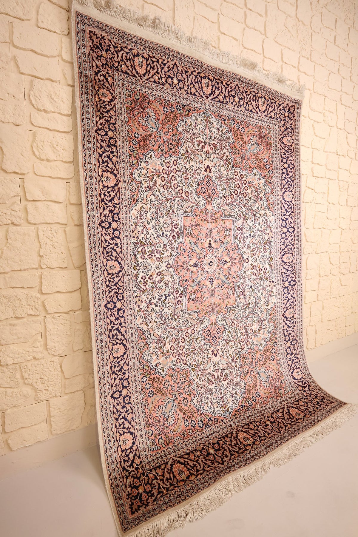 Vue de biais du tapis Cachemire rose et bleu, champ ivoire fleuri et bordure bleu nuit