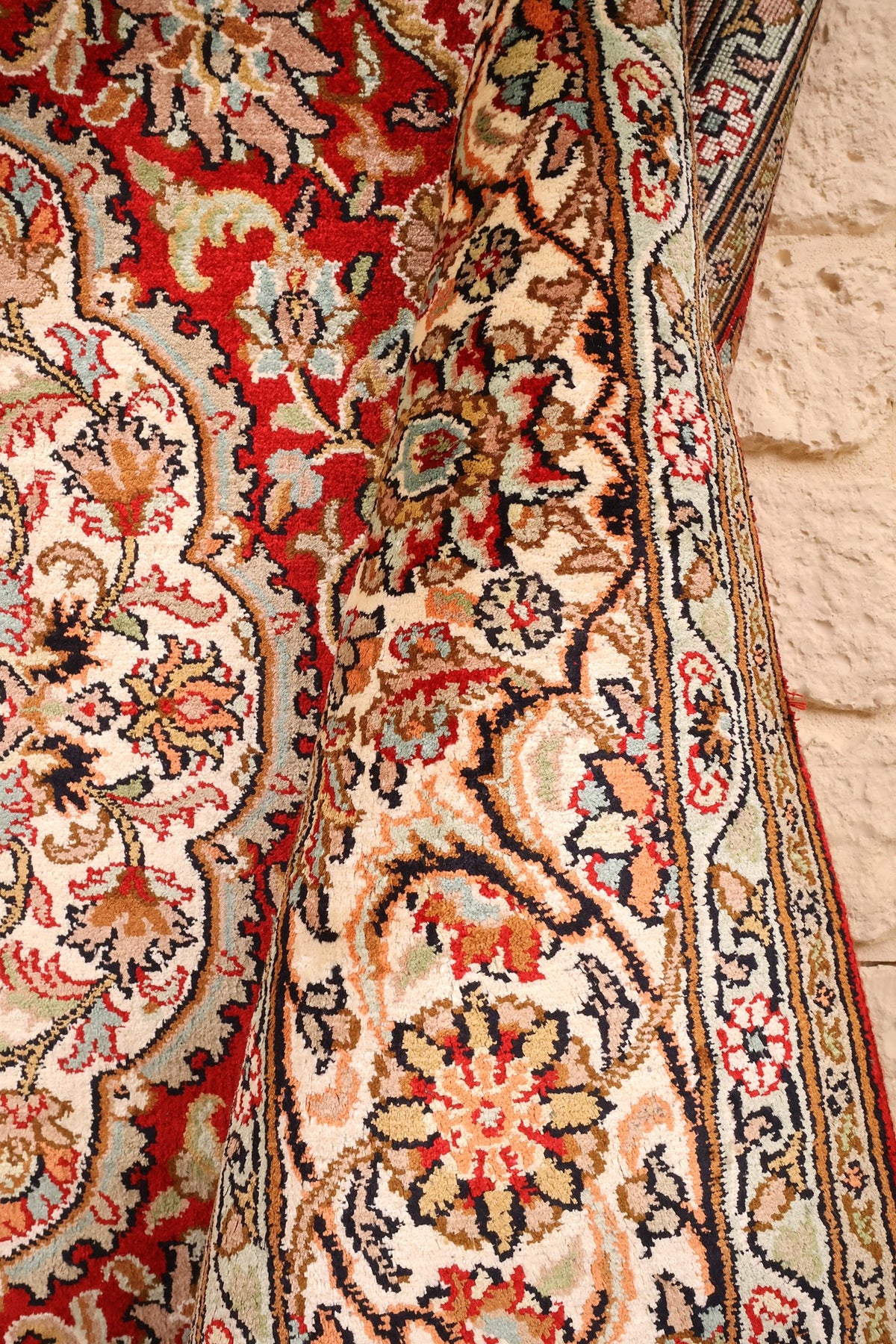 Coin replié du tapis Cachemire rouge et beige, bordure et champ fleuri côte à côte