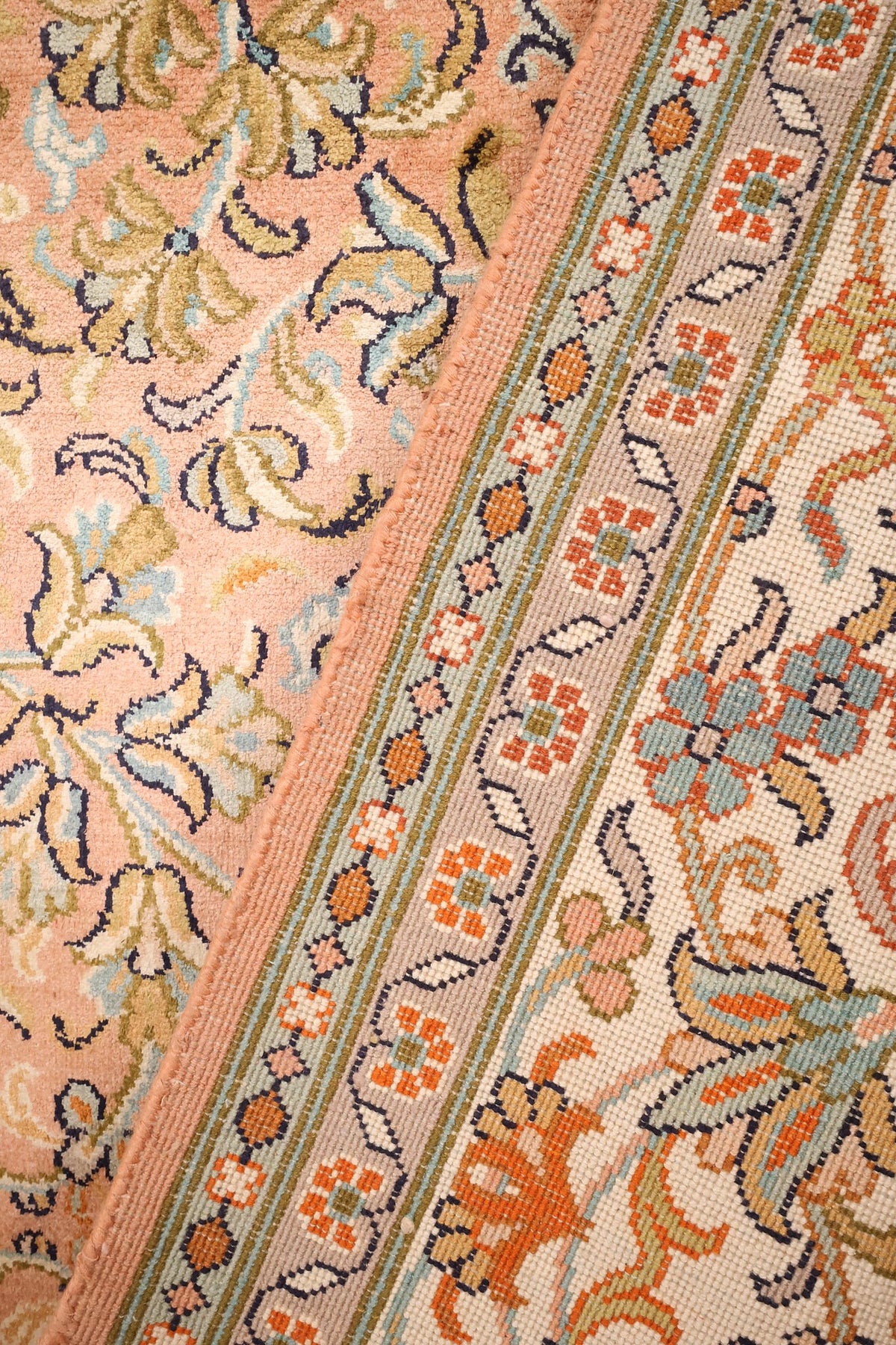 Gros plan du tapis Cachemire noué main, passage du champ rose à la bordure fleurie