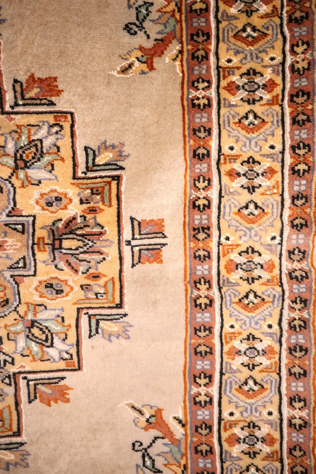 Bordure jaune à rosettes et losanges, filets noirs et blancs du tapis Caucase beige