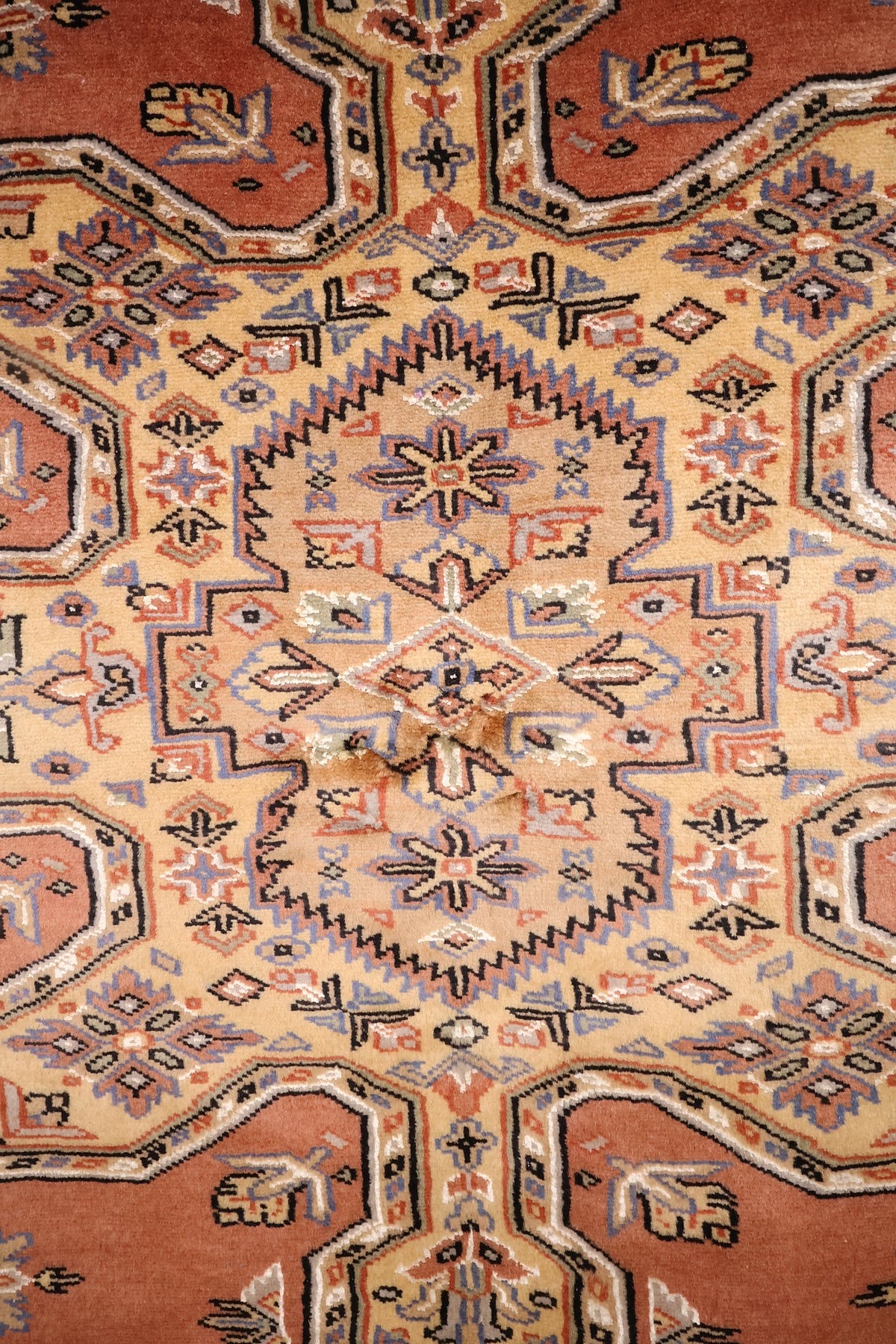 Détail du médaillon étoilé beige et des rosettes bleues du tapis Caucase rose