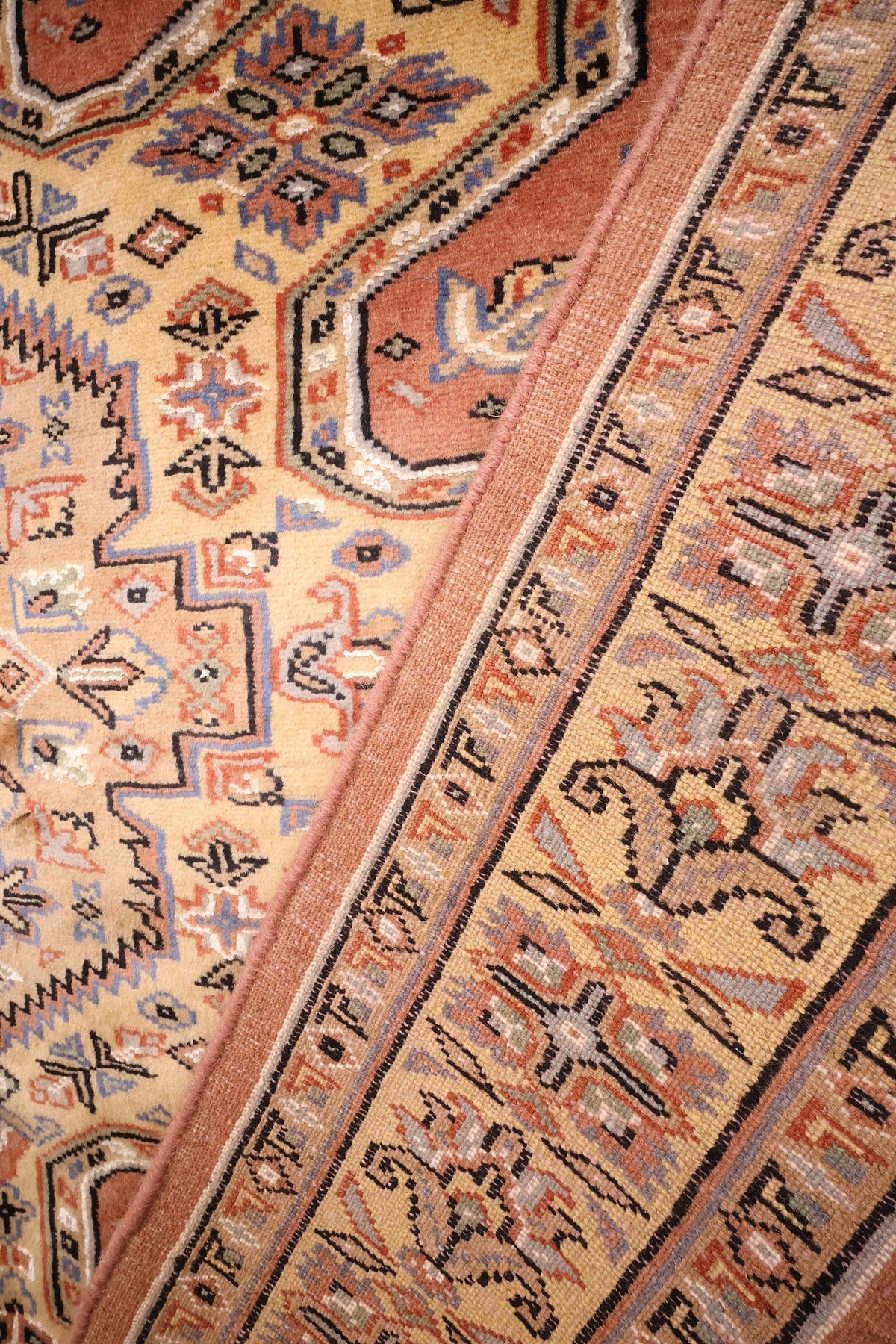 Bordure vue de biais, rinceaux beige et crochets bleus du tapis Caucase en laine