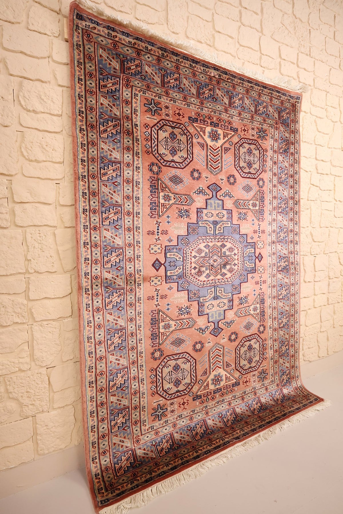 Tapis Caucase rose en laine, vue de biais révélant les étoiles et les franges blanches