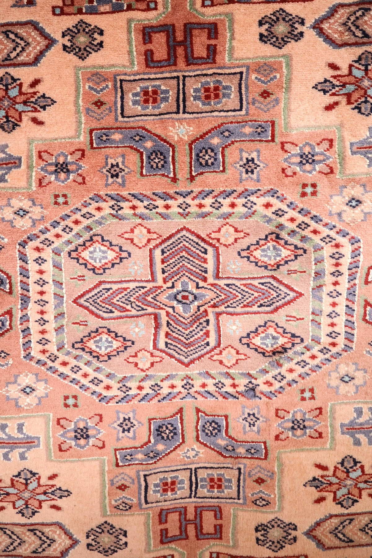 Détail du médaillon octogonal à crochets sur champ rose saumon du tapis Caucase