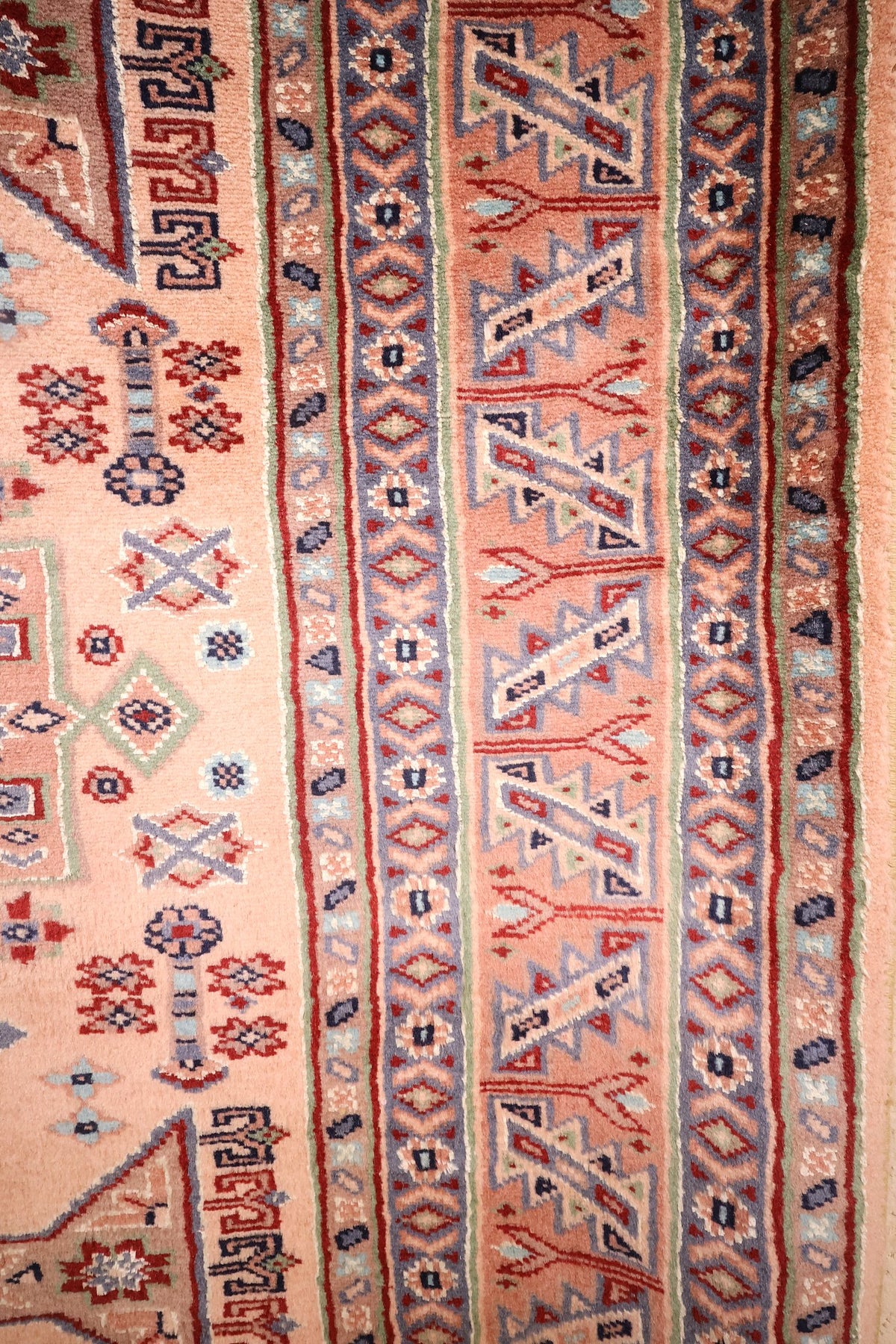 Bordures du tapis Caucase : chevrons bleus et galons à rosettes sur fond saumon