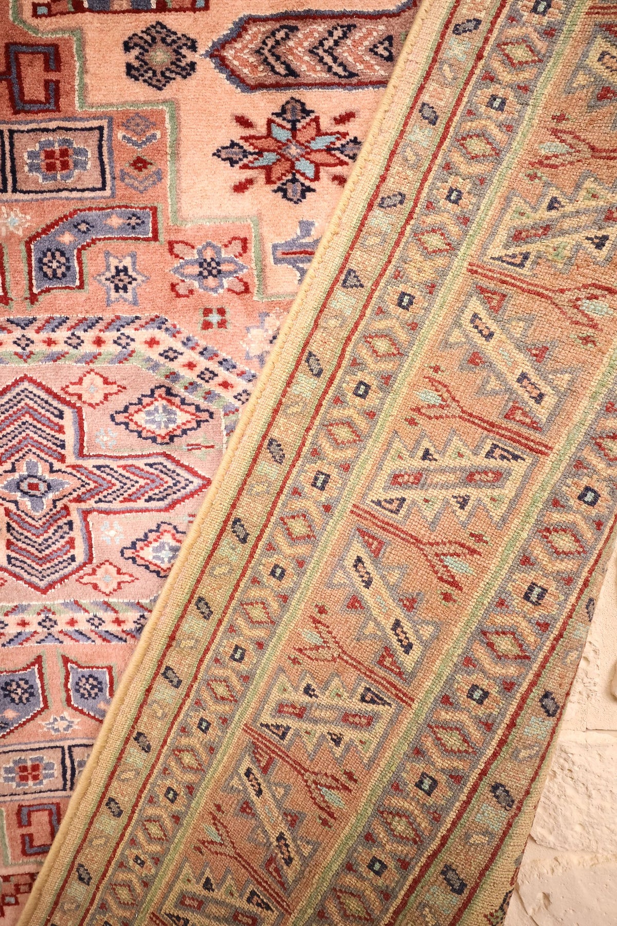Coin replié du tapis Caucase rose, épaisseur de la laine et bordure visibles