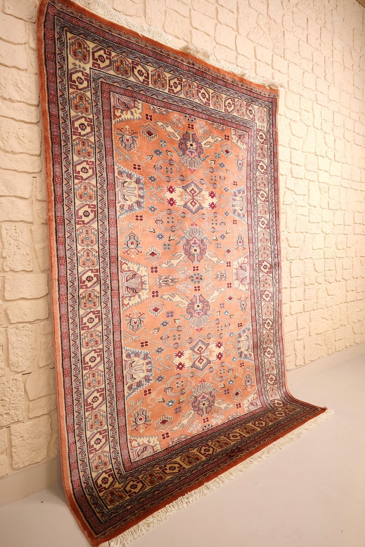 Tapis Caucase en laine noué à la main, vue de biais contre un mur clair