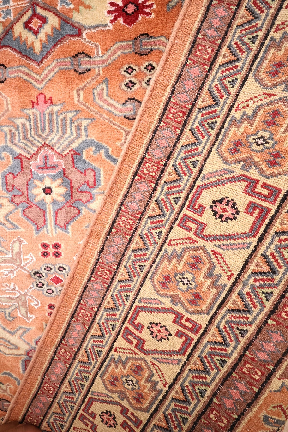Bordure vue en diagonale, palmettes ivoire et filets noirs du tapis Caucase orange