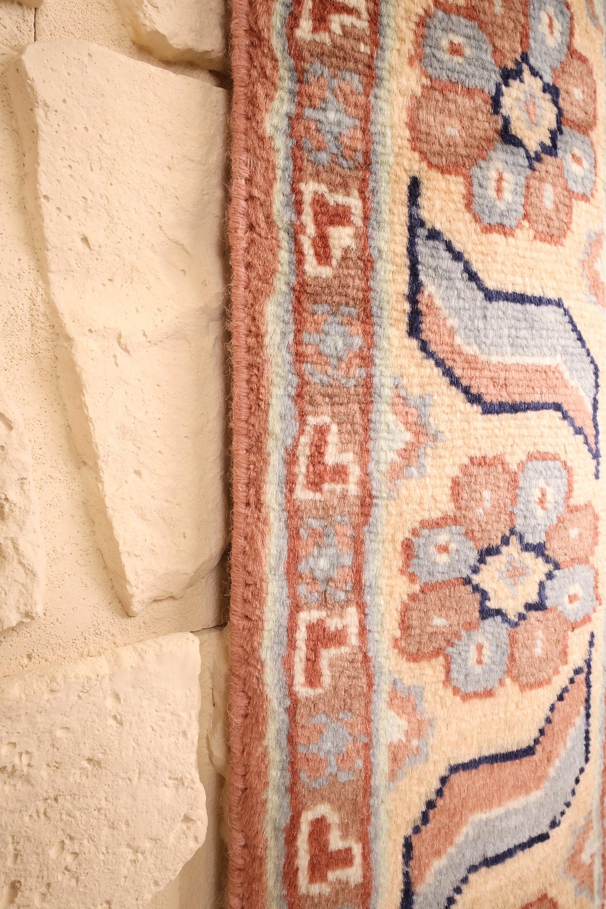 Lisière du tapis Caucase rose contre un mur de pierre, bordure beige fleurie
