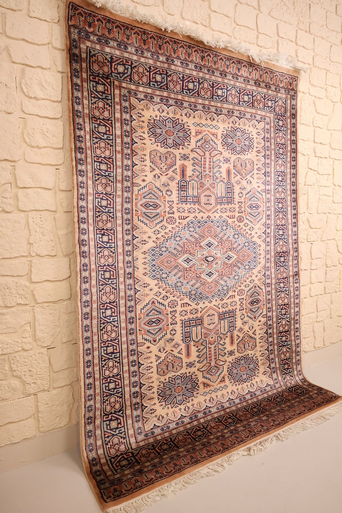 Tapis Caucase en laine noué à la main, vue de biais contre un mur clair