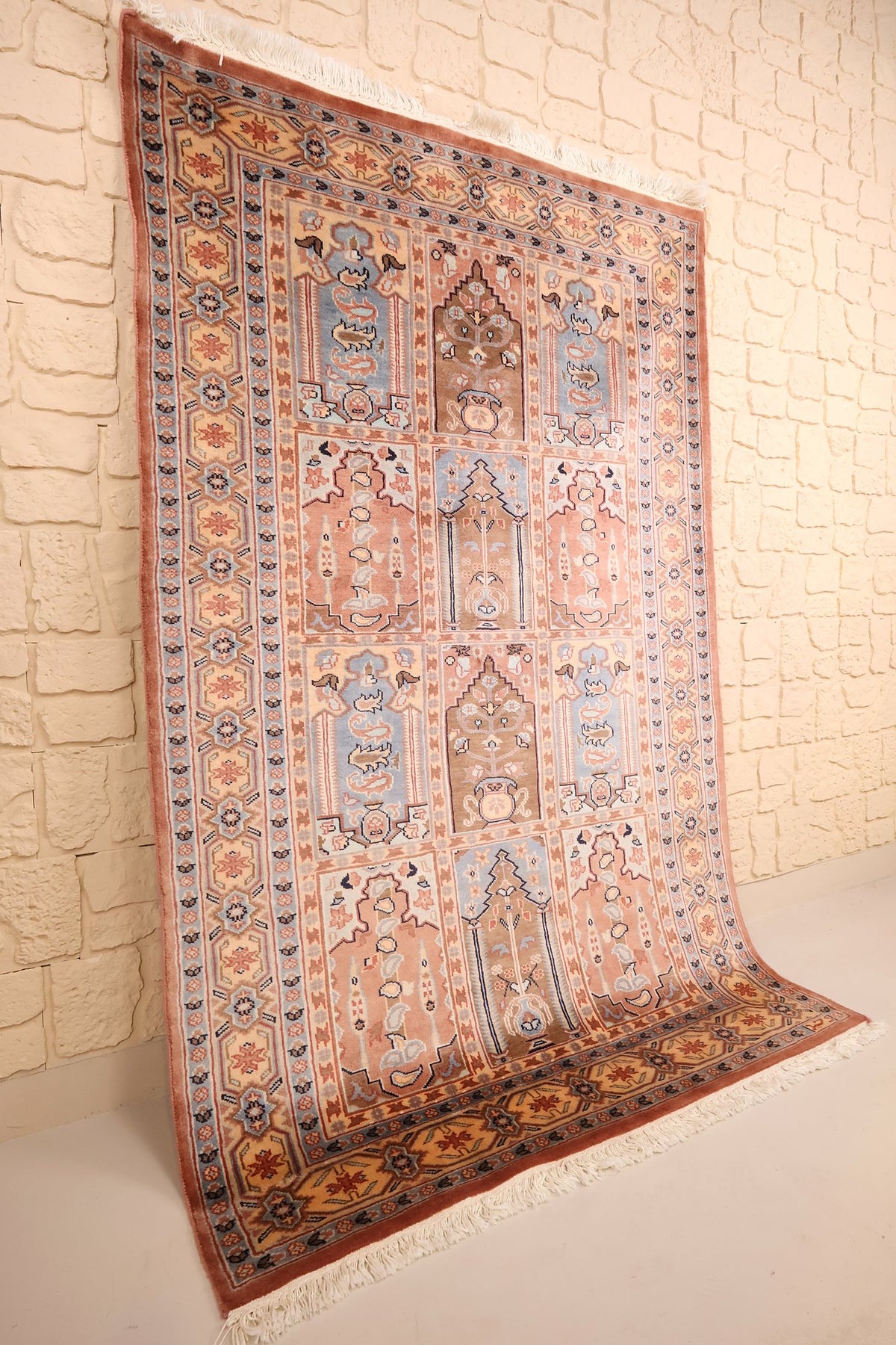 Vue de biais du tapis rose, beige et bleu, champ compartimenté et large bordure