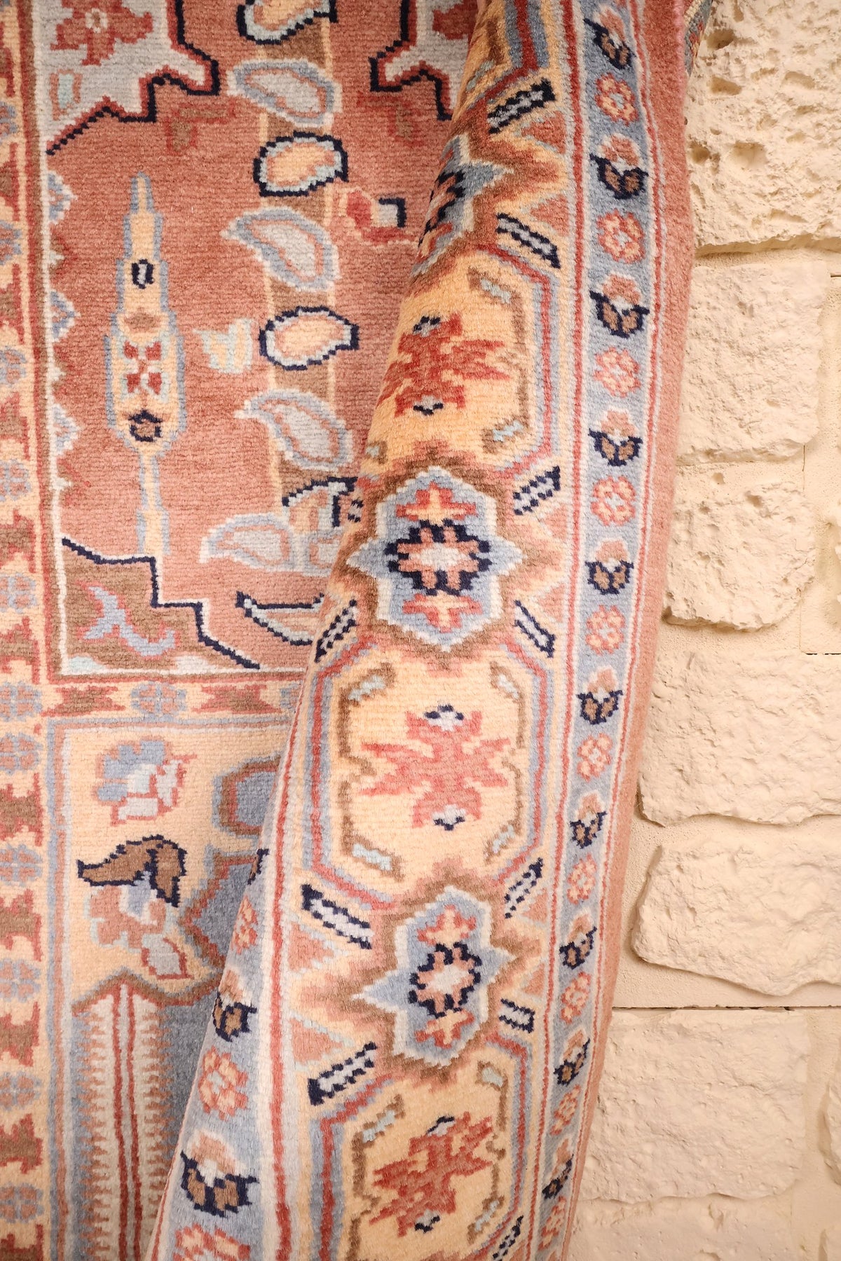 Lisière du tapis rose relevée, bordure à rosaces et crochets bleu nuit