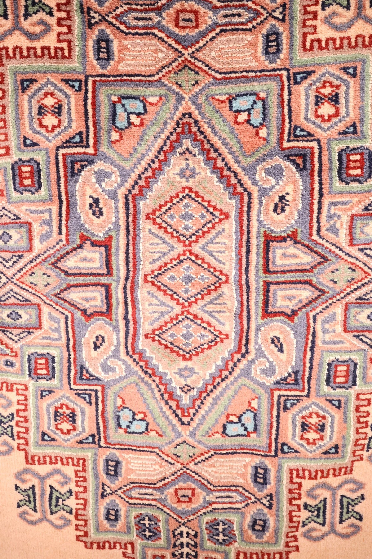 Détail du médaillon anguleux crénelé en bleu-gris, rouge et vert pâle du tapis Caucase