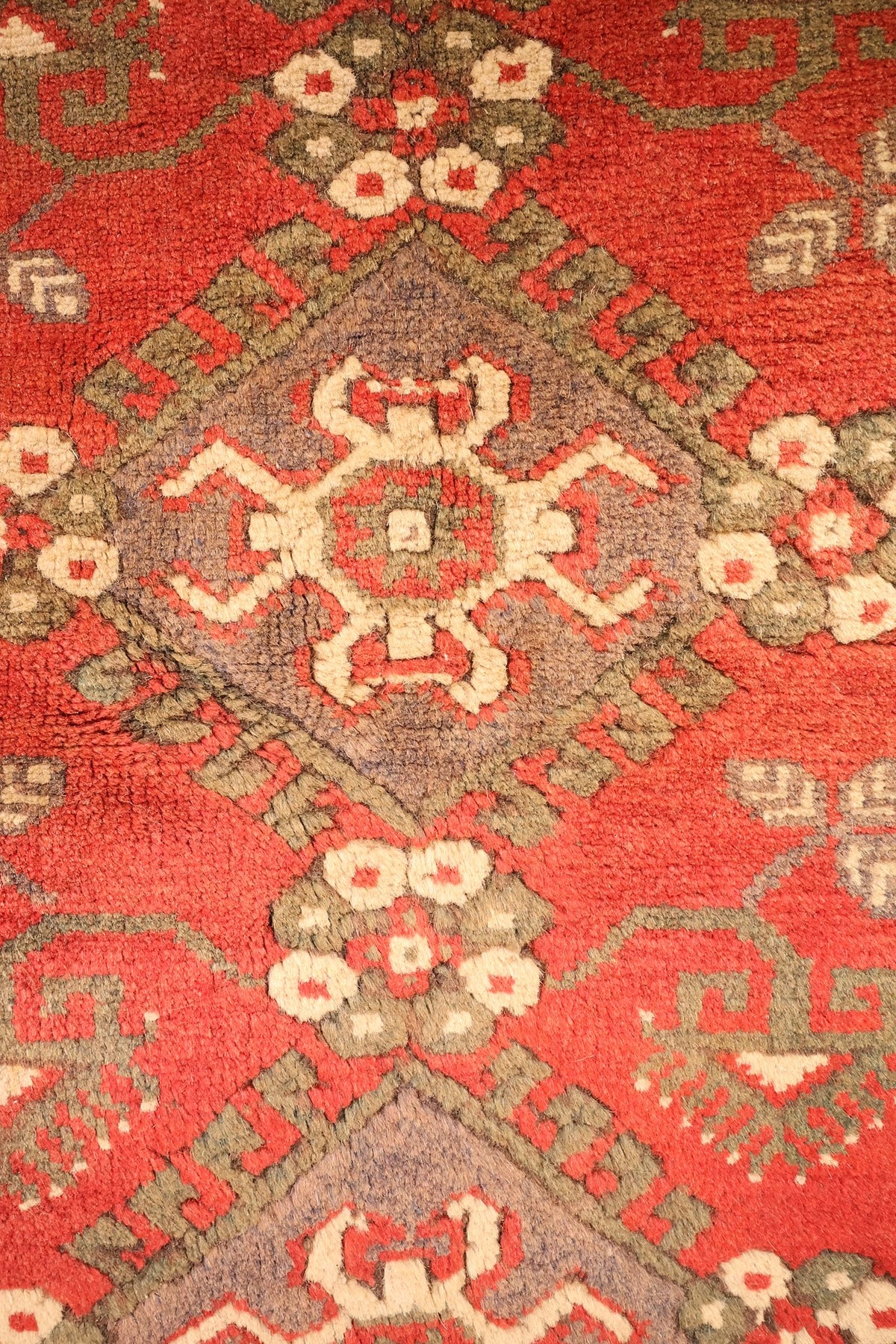 Détail du médaillon crénelé mauve et vert aux rosettes crème du tapis Dodgem Alti rouge