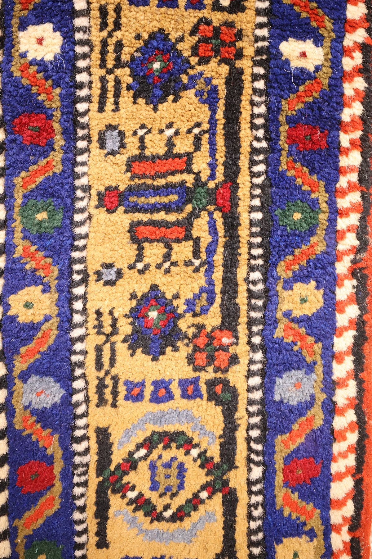 Bordure jaune ocre du tapis Dodgem Alti, bandes bleues et galons en damier noir et blanc