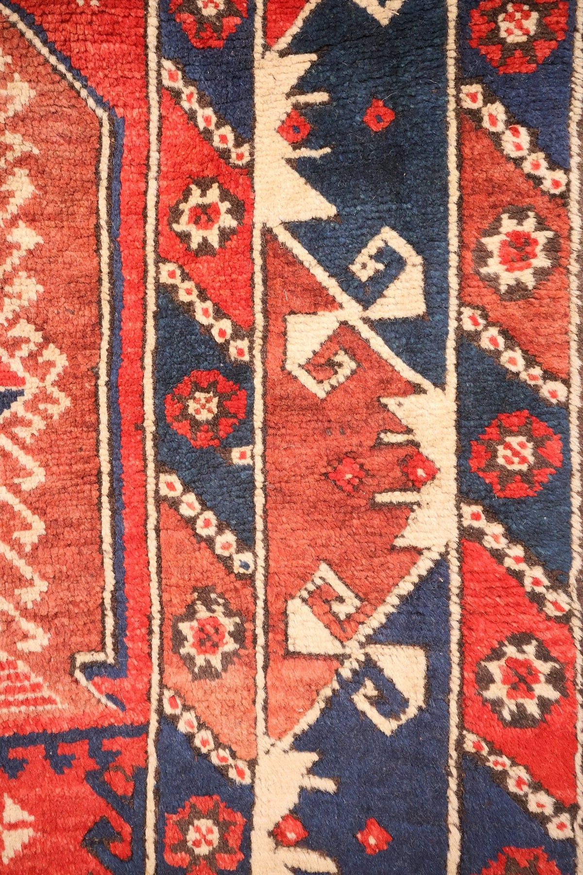 Bordures du tapis Dodgem Alti : rosettes étoilées, crochets et chevrons crème sur bleu et rouge