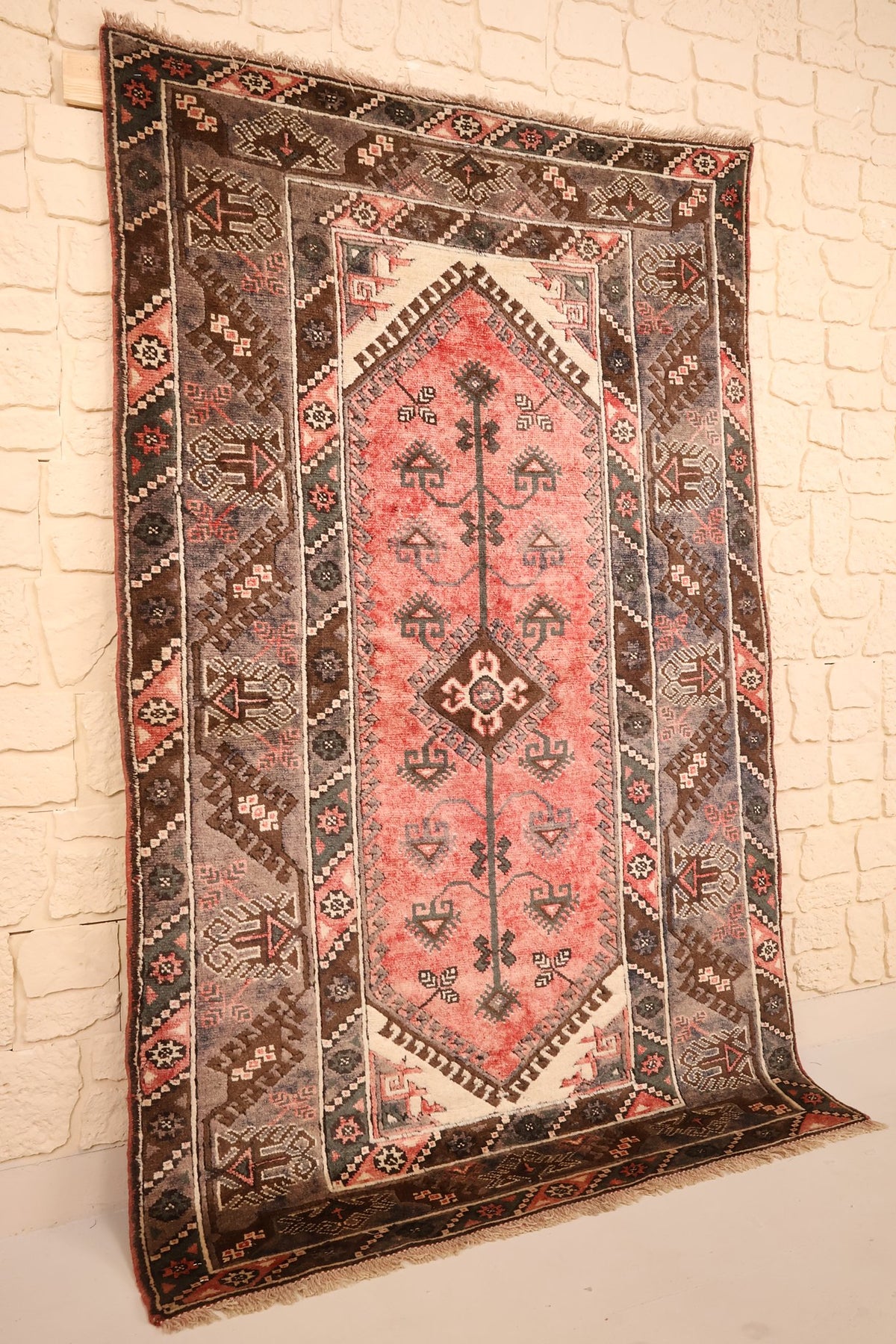 Tapis Dodgem Alti rectangulaire rose et marron vu de biais contre un mur clair