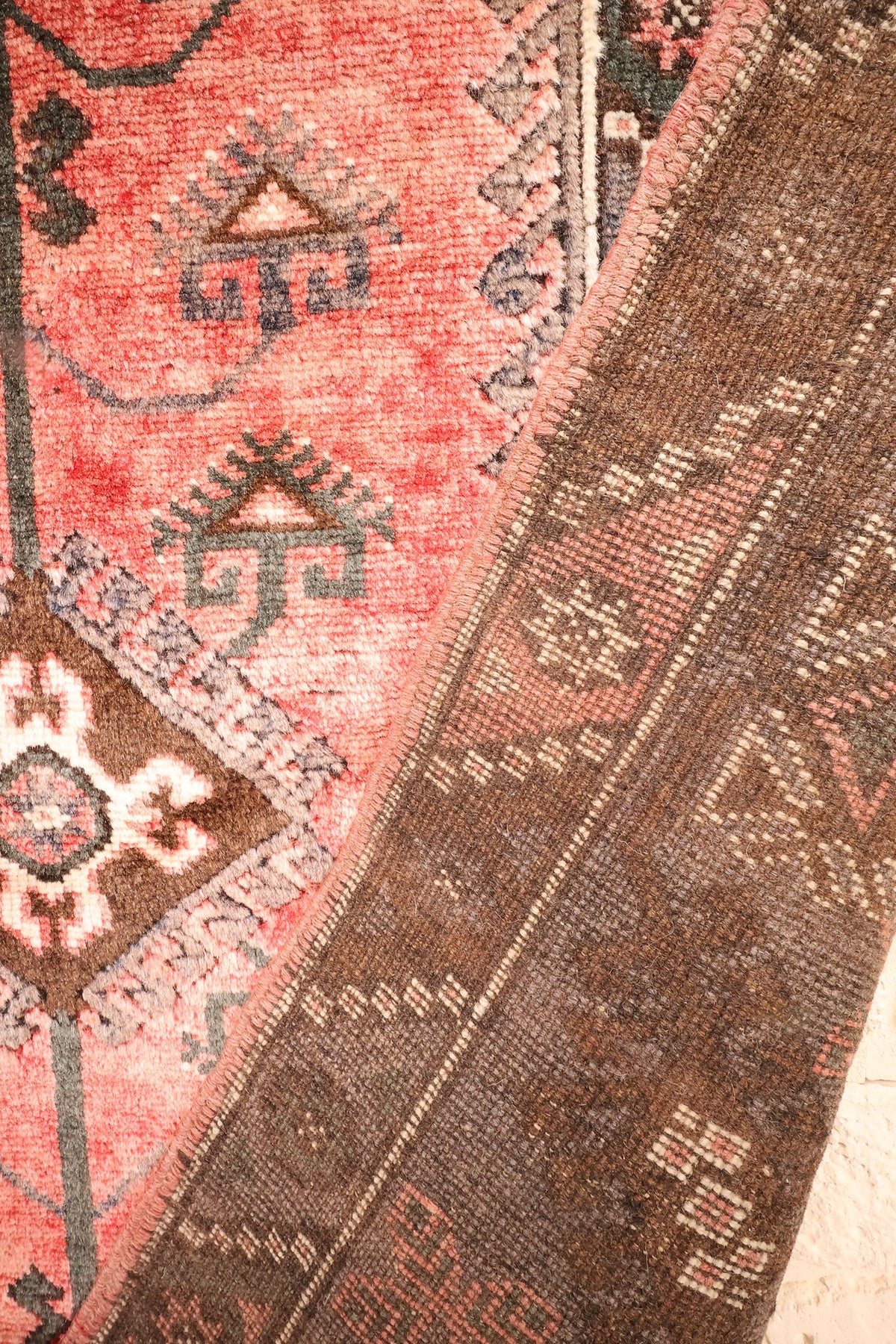 Coin replié du tapis Dodgem Alti, motifs crochetés gris-vert près de la bordure marron