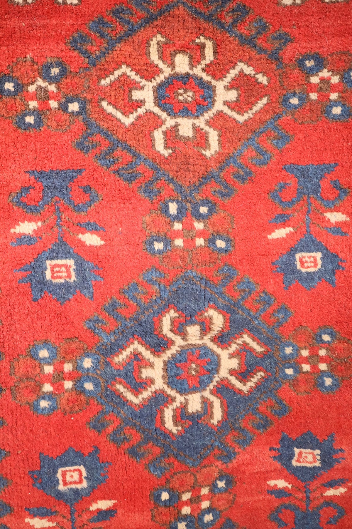 Détail des rosettes anguleuses ivoire et bleu sur le champ rouge du tapis Dodgem Alti