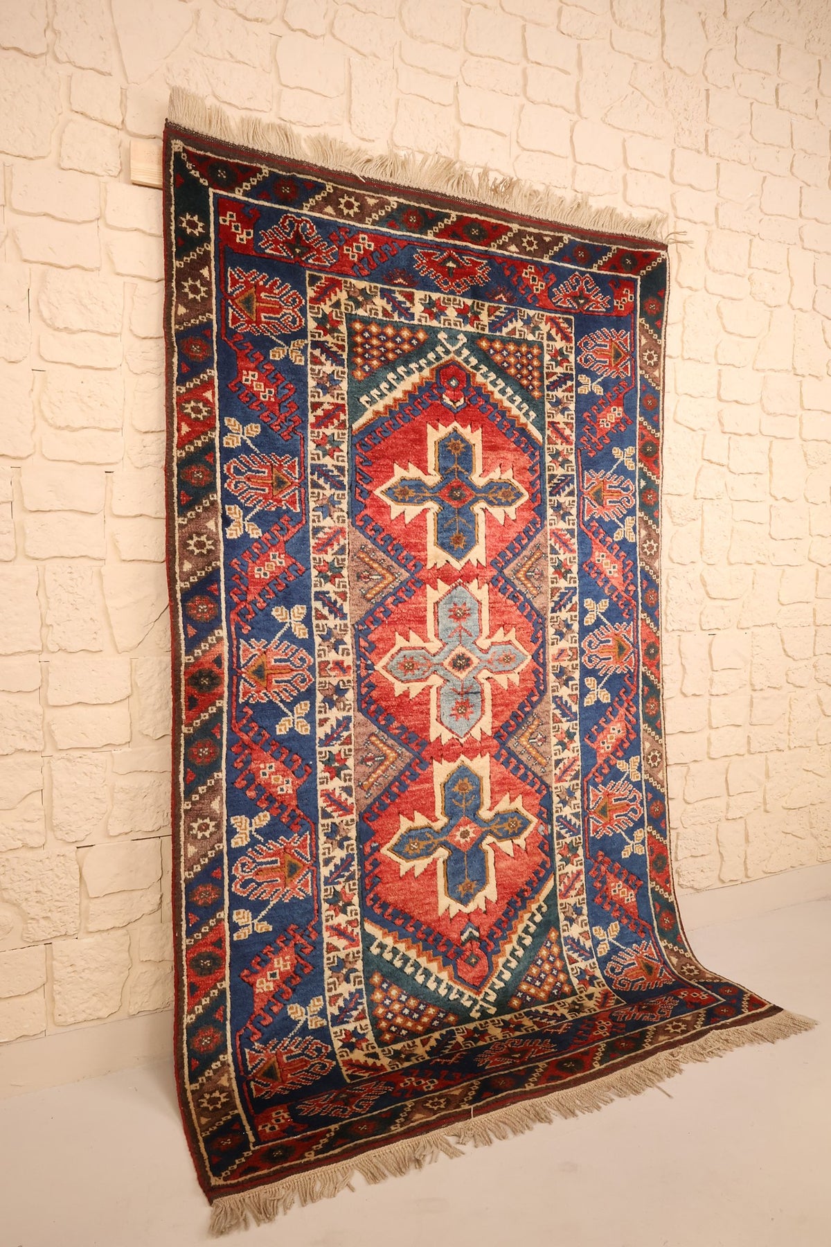 Vue de biais du tapis Dodgem Alti rectangulaire rouge brique à bordure bleue et franges écrues