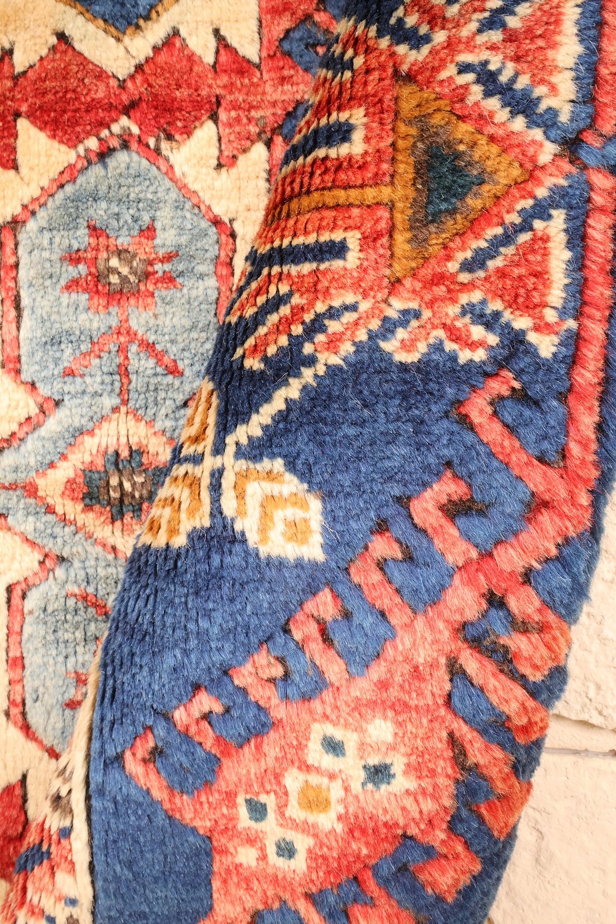 Coin replié du tapis Dodgem Alti rouge et bleu, épaisseur et dessin de la bordure visibles