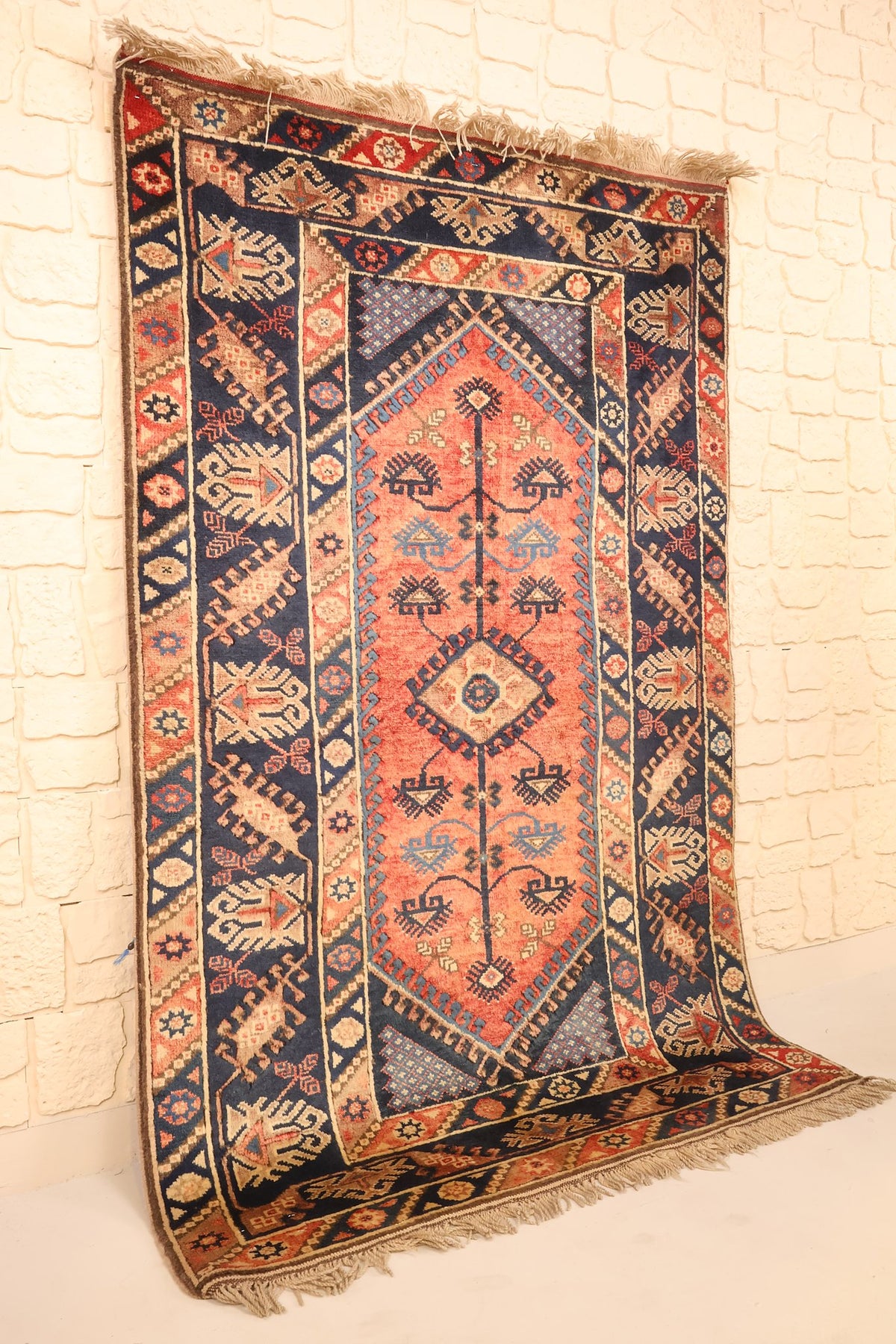 Vue de biais du tapis Dodgem Alti rectangulaire 197 × 123 cm, champ rouge orangé et bordures bleu nuit