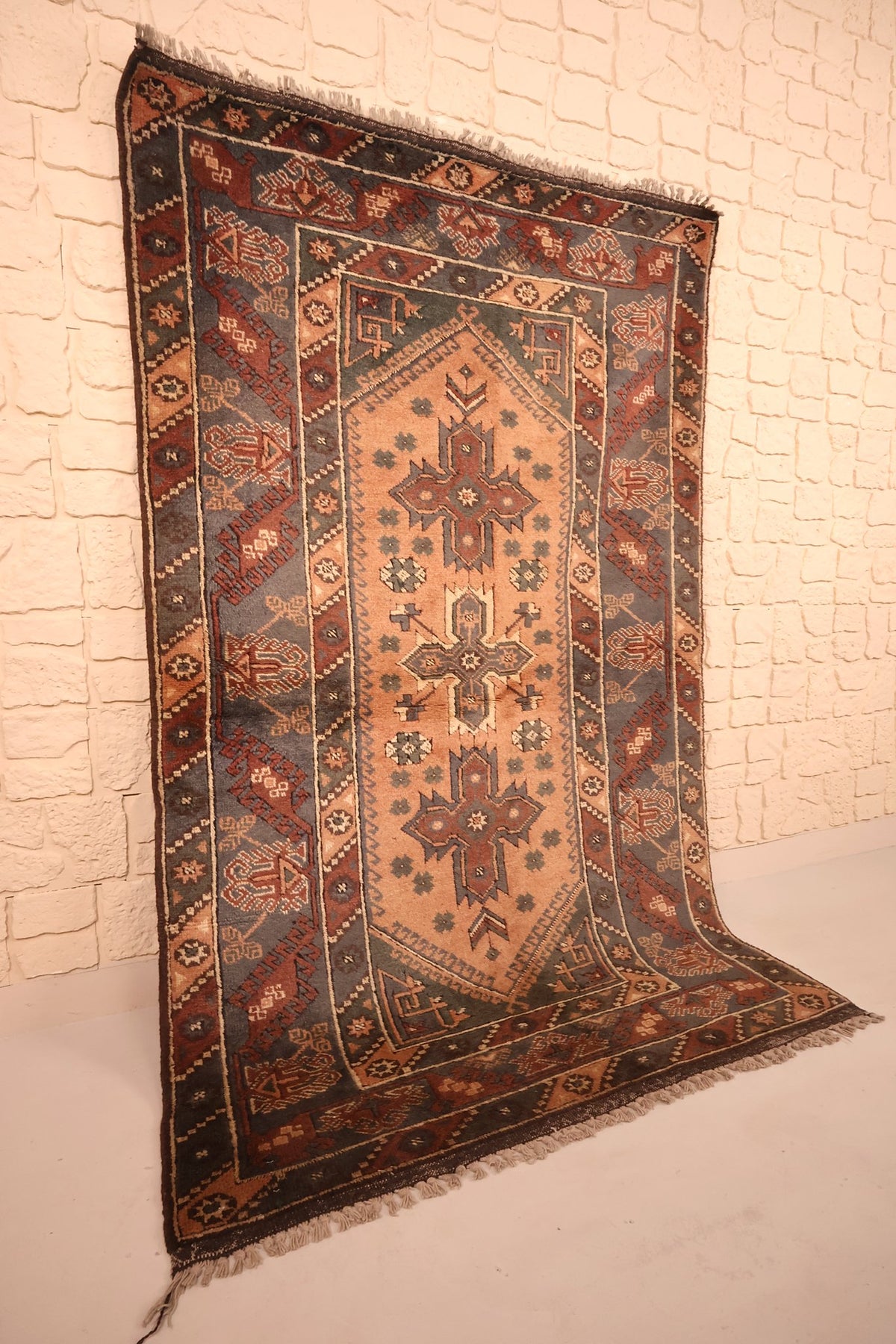 Vue de biais du tapis Dodgem Alti en laine, champ beige rosé et bordure gris-bleu