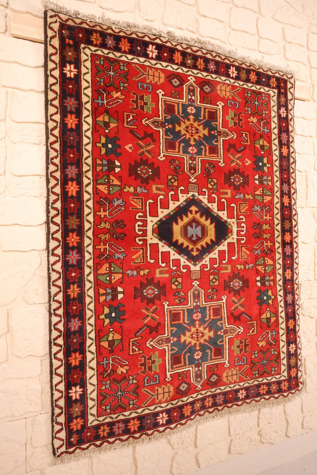 Tapis Garadgeh en laine nouée à la main, vue de biais sur le champ rouge et sa bordure bleue