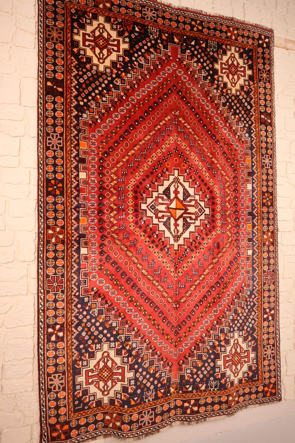 Vue de biais du tapis Gashgaï en laine, médaillon ivoire et angles bleu nuit
