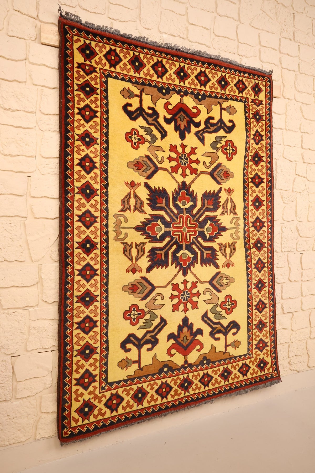 Tapis Ghazni en laine à champ jaune doré, vue de biais sur le mur