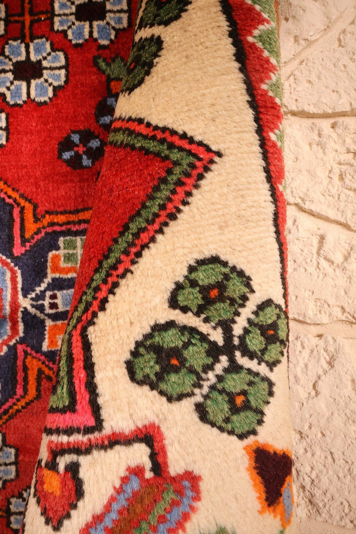 Coin relevé du Hamadan rouge, rosettes vertes sur fond crème en gros plan