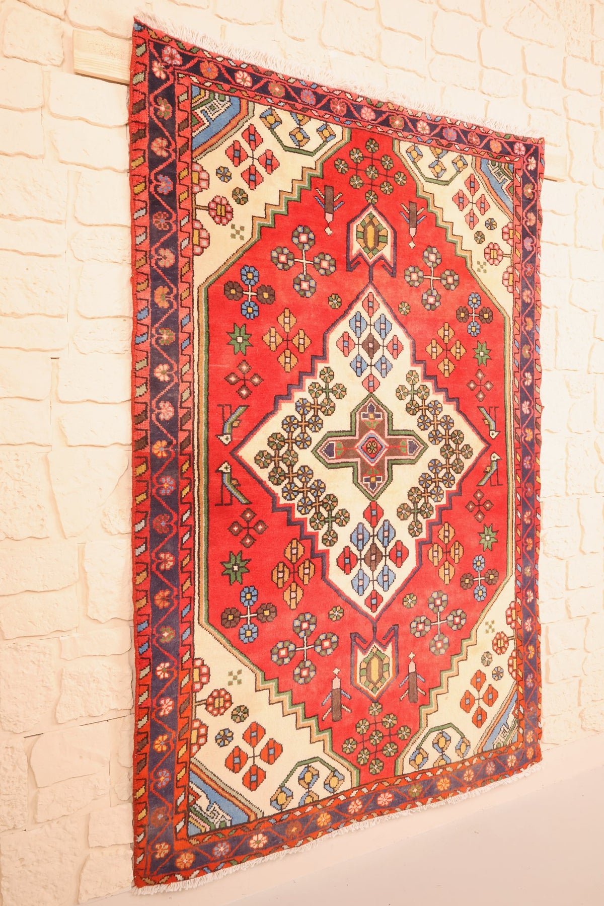 Tapis Hamadan rouge et bleu vu de biais, bordure fleurie et franges blanches