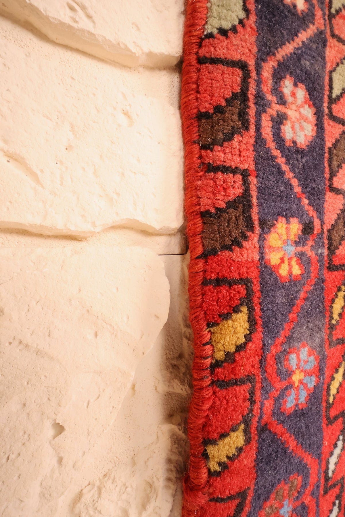Lisière du tapis Hamadan rouge, bord noué à la main contre un mur clair