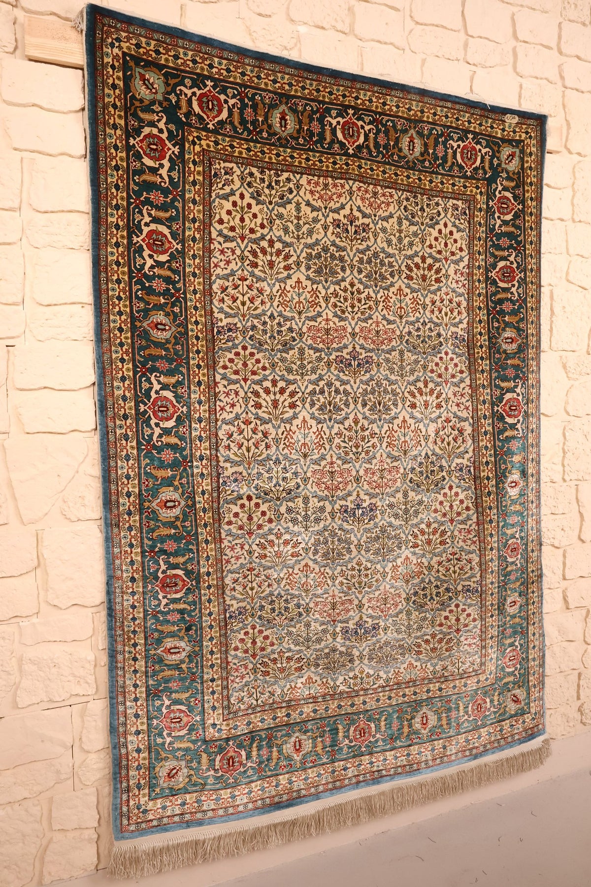 Tapis Hereke beige et vert vu de biais, champ fleuri et bordures vert-bleu