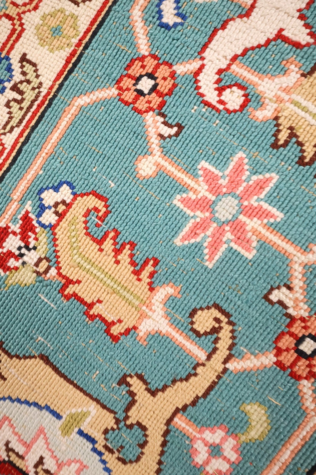 Gros plan des palmettes et rosaces rouges sur fond vert-bleu du tapis Hereke